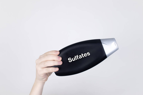 シャンプーラベルの化学成分:硫酸塩。女性の手は有害成分を示す瓶を保持します。白い背景、テキストの場所 - 写真・画像