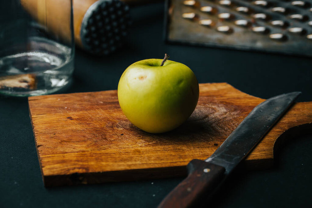 Ένα κοντινό πλάνο ενός ολόκληρου ώριμου πράσινου μήλου σε ένα ξύλο κοπής με ένα μαχαίρι πάνω του. - Φωτογραφία, εικόνα