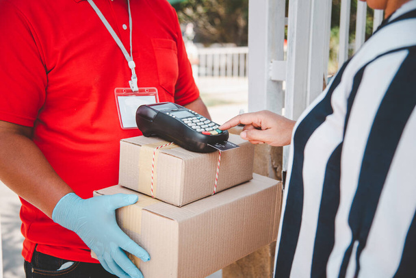 Male delivery workers wear sanitation faces and wear gloves, deliver goods or parcels, delivery service for users to pay via credit card for convenience and forgiveness during covid19. - Photo, Image