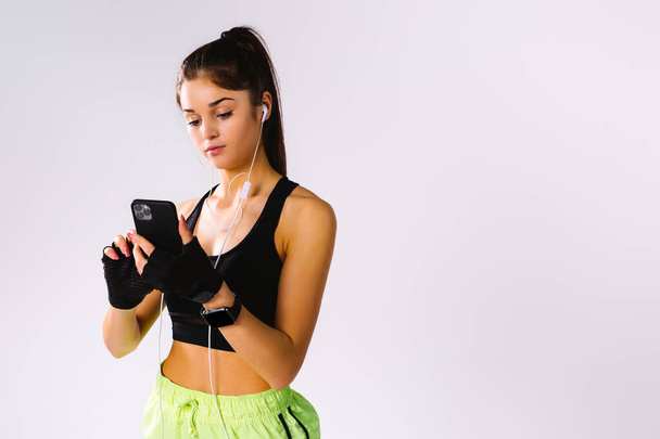 Young brunette in a top and shorts with a phone and headphones on a white background with empty side space. - Photo, Image