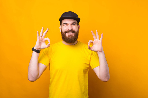 Foto de un joven alegre con camisa amarilla mostrando el gesto OK y sonriendo a la cámara - Foto, imagen