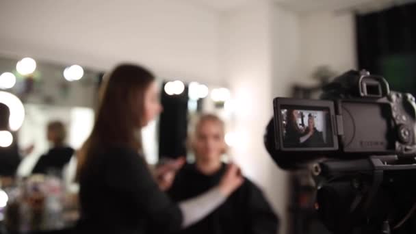 Vrouw make-up voor aantrekkelijke blonde haar vrouw in de studio. Selectieve focus van digitale camera met make-up kunstenaar toepassen van cosmetica voor mooi model. Vlog - Video