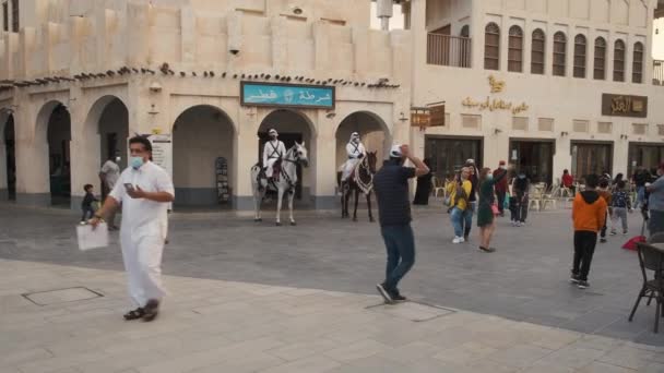 Souq Waqif Doha Katar főutcájában, napnyugtakor közeledik és fotózkodik, bemutatva a régi rendőrőrsöt, ahol hagyományos rendőrök lovagolnak, helyiek és látogatók sétálnak. - Felvétel, videó