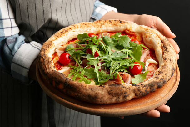 Woman holding tasty pizza with meat and arugula on black background, closeup - Foto, imagen