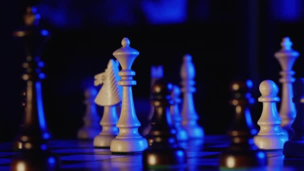 Houten schaakstukken op een schaakbord in een donkere kamer met blauwe achtergrondverlichting - Video