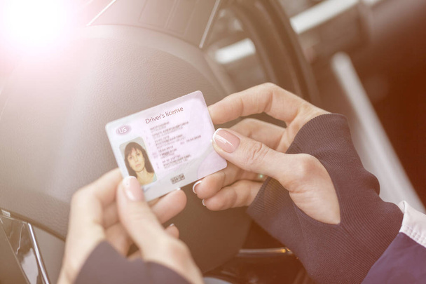 Jogosítványt szerezve, női kezek mutatják az amerikai jogosítványt, egy autó kormánya között, tónusos - Fotó, kép