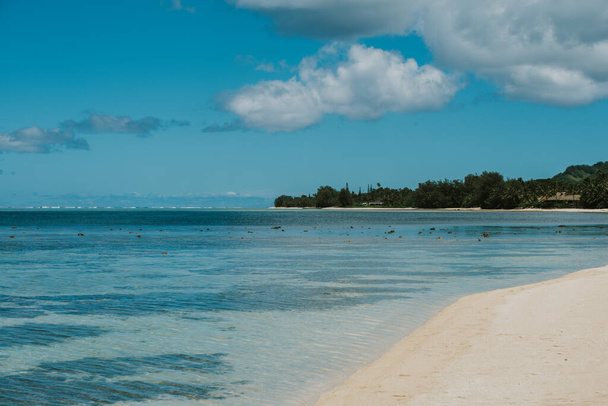 Άποψη μιας όμορφης τροπικής παραλίας με λευκή άμμο, φοίνικες, τυρκουάζ ωκεανό με σύννεφα την ηλιόλουστη μέρα του καλοκαιριού. Τέλειο φόντο τοπίο για χαλαρωτικές διακοπές, Ραροτόνγκα, Νήσος Κουκ. - Φωτογραφία, εικόνα