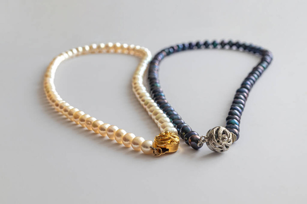 Dwa perłowe naszyjniki, z białymi i ciemnoniebieskimi perłami, z metalowymi zapięciami, na jasnym tle - Zdjęcie, obraz