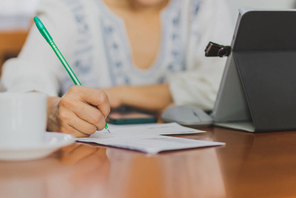 Vrouwelijke hand schrijven op financiële papieren tijdens het betalen van rekeningen online met behulp van laptop. - Foto, afbeelding