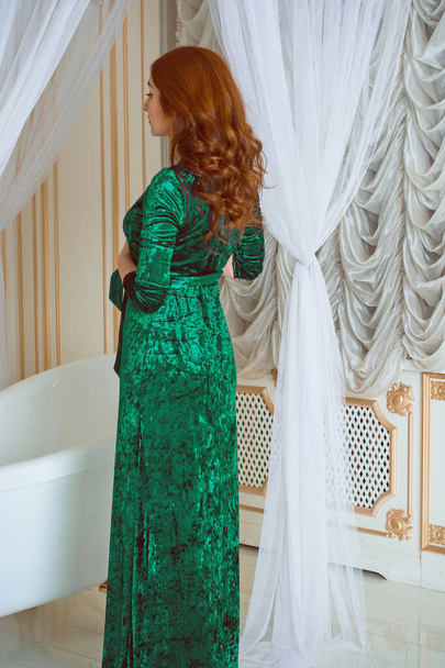 Runsas nainen viktoriaaniseen tyyliin sisustus, pukeutunut sametti vihreä pitkä smaragdi vaahtoava puku. Käsite naisellisuus ja houkuttelevuutta - Valokuva, kuva