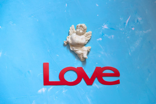 Valentines day card with  figurine of little Cupid holding heart, love angel and word Love  on blue background. Concept Valentine's Day Template Gr. Romance holiday amur boy character.  - Photo, Image