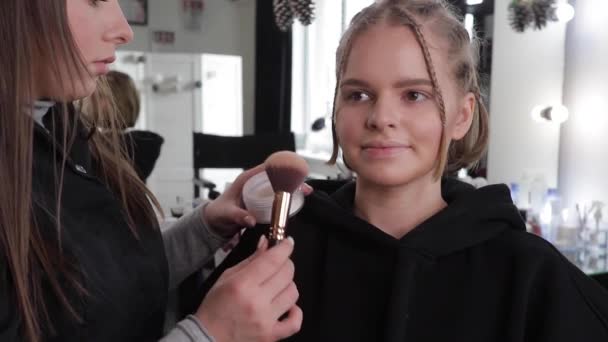 Γυναίκα κάνει μακιγιάζ για ελκυστική ξανθιά γυναίκα μαλλιά στο στούντιο. Βίντεο από makeup artist εφαρμογή καλλυντικών για όμορφο μοντέλο. Ψηφιακή κάμερα κάνει βίντεο για vlog - Πλάνα, βίντεο
