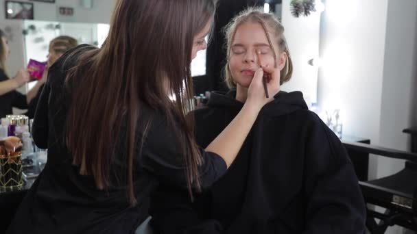 Woman make makeup for attractive blond hair woman in studio. Video of makeup artist applying cosmetics for beautiful model. Digital camera make video for vlog - Footage, Video