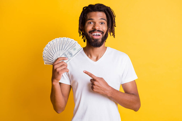 Photo of young black bearded guy dreadlocks hold indicate finger income cash fan wear white t-shirt isolated yellow color background - Photo, image