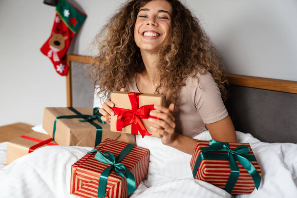 Happy nice woman smiling and opening gift boxes while sitting in bed at home - Fotografie, Obrázek