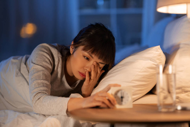 asian woman with clock lying in bed at night - Foto, immagini