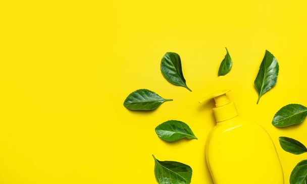 Natural organic cosmetics. Beauty, spa, branding mockups. Yellow cosmetic bottle container fresh green leaves on yellow background flat lay top view. Minimalistic concept of packaging eco cosmetics - Fotoğraf, Görsel