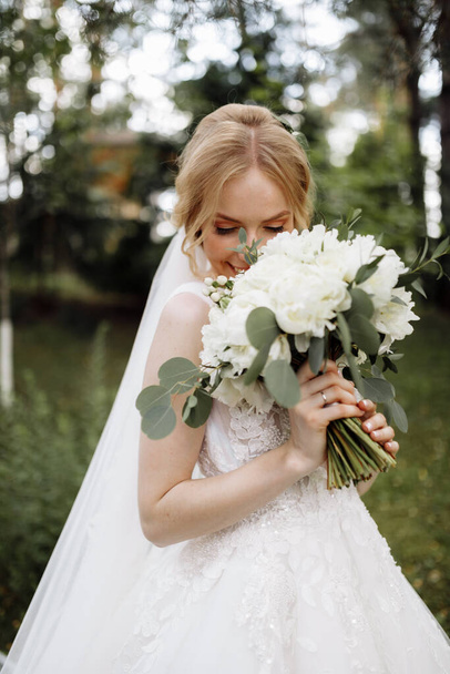 menyasszony egy ruha áll egy zöld kertben, és kezében egy esküvői csokor virágok és zöldség. Kiváló minőségű fénykép - Fotó, kép