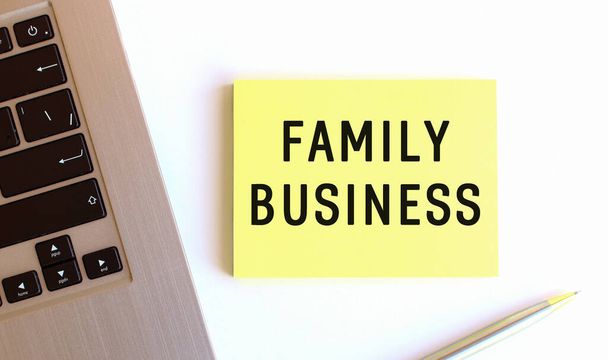 De inscriptie FAMILY BUSINESS op de gele sticky notes in de buurt van de laptop op het witte bureau. - Foto, afbeelding