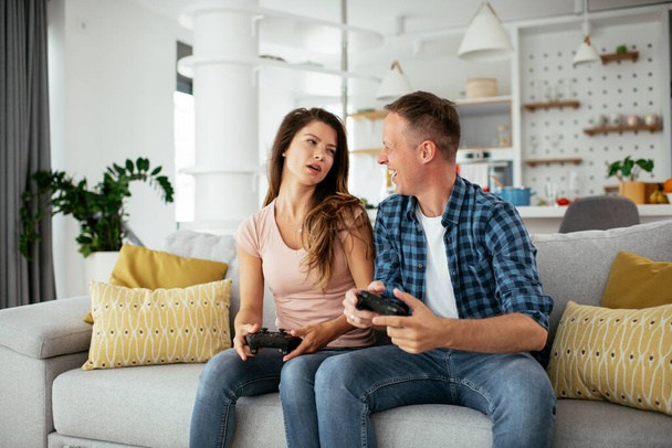 Boyfriend and girlfriend playing video game with joysticks in living room. Loving couple are playing video games at home. - Foto, Bild