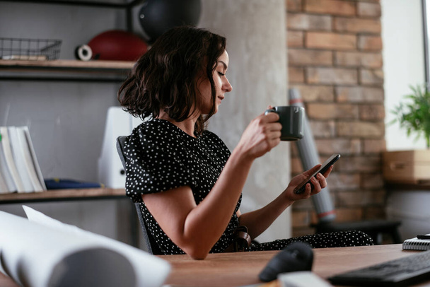 Empresária usando smartphone durante o freio de café enquanto trabalhava no escritório - Foto, Imagem
