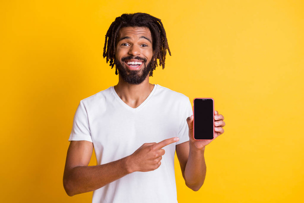 Photo of black guy beard dreadlocks indicate finger hold showing telephone touchscreen empty space wear white t-shirt isolated yellow color background - Photo, image