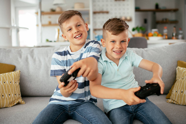 Щасливі брати грають у відеоігри. Молоді брати розважаються, граючи у відеоігри у вітальні
 - Фото, зображення