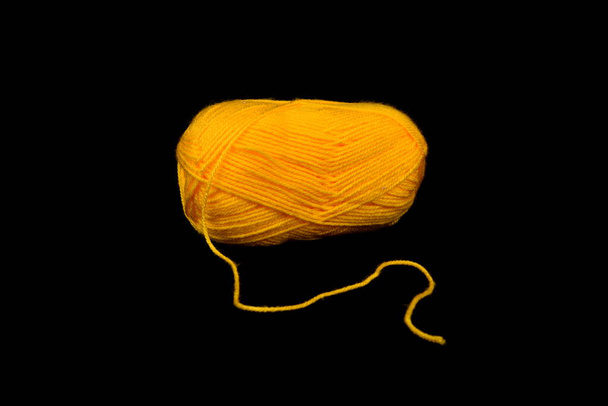 Una palla di filato giallo su sfondo nero. Palla di lana dorata  - Foto, immagini