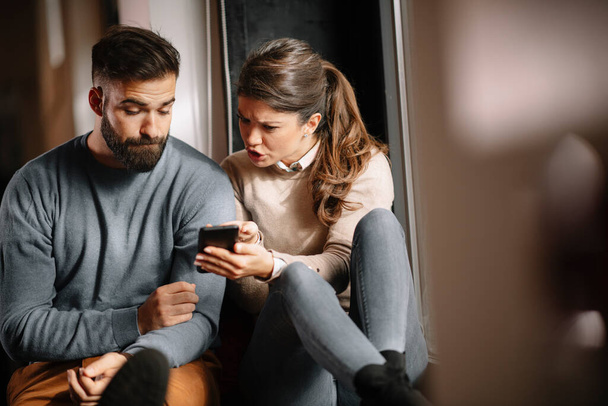 自宅で携帯電話のための怒っているカップルや結婚の戦い。スマートフォンを持っている嫉妬深い女性と彼の夫にメッセージを示す - 写真・画像