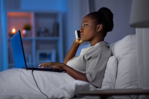 woman with laptop calling on smartphone in bed - Photo, Image