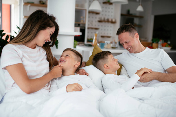 Familia joven disfrutando en la cama. Padres felices con hijos relajándose en la cama. - Foto, Imagen