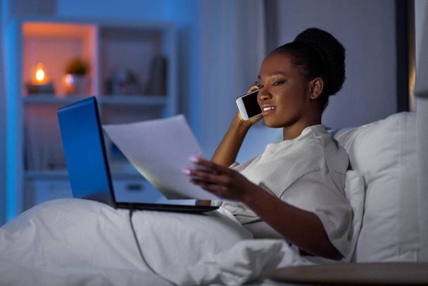 женщина с ноутбуком звонит на смартфон в постели - Фото, изображение
