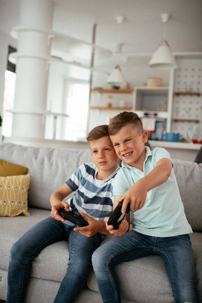 Onnelliset veljet pelaamassa videopelejä. Nuoret veljet hauskaa pelatessaan videopelejä olohuoneessa - Valokuva, kuva