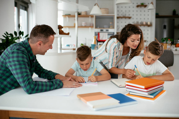 Οι γονείς βοηθούν τα παιδιά με τις εργασίες τους. Μικρά αγόρια μαθαίνουν στο σπίτι. - Φωτογραφία, εικόνα