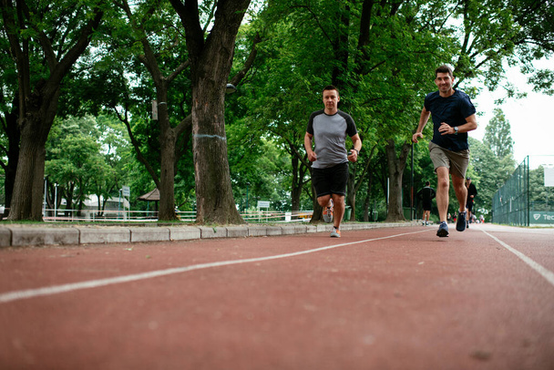 Young men training on a race track. Two young friends running on athletics track - Photo, Image