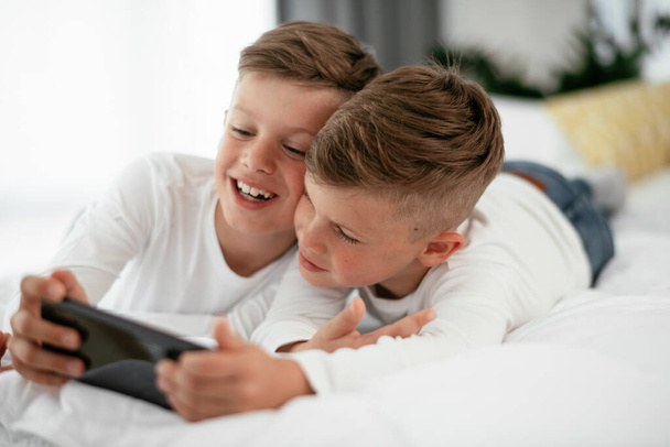 Two little brothers are playing games on the phone. Beautiful boys enjoying at home. - Valokuva, kuva