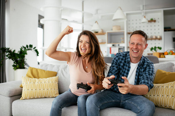 Boyfriend and girlfriend playing video game with joysticks in living room. Loving couple are playing video games at home. - Photo, Image
