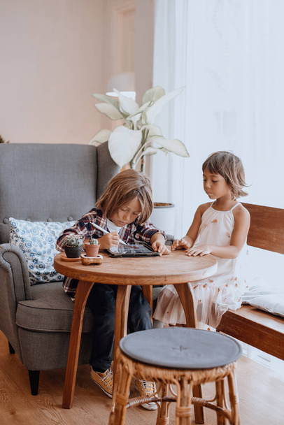 Niño y niña con lápiz digital y tableta en la mesa en la sala de estar - Foto, Imagen