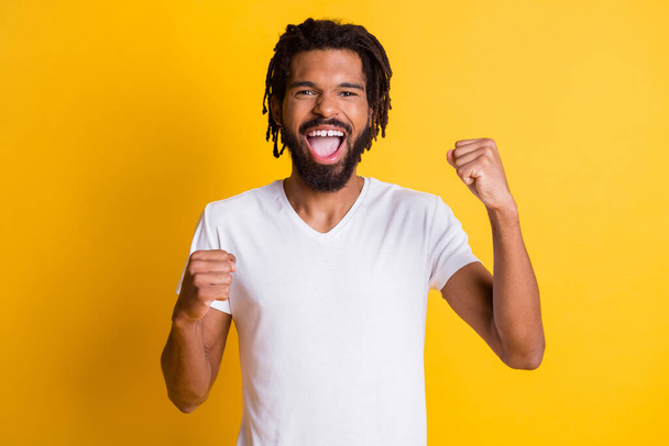 Photo of ecstatic dark skin model guy raise fists celebrate goal wear casual t-shirt isolated yellow color background - Fotoğraf, Görsel