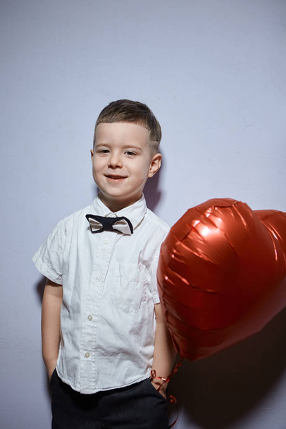 Na Valentýna. Šťastný chlapec stojí a drží červené koule srdce na bílém pozadí.  - Fotografie, Obrázek