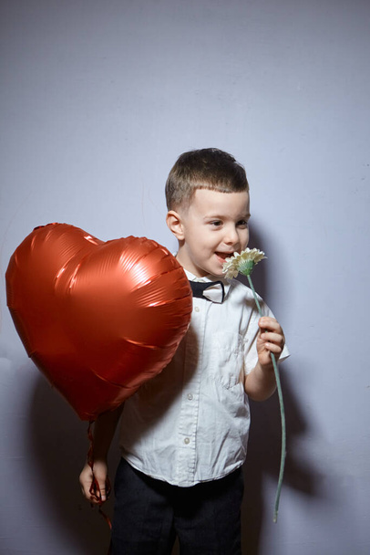 Valentine's day. Happy boy stands and holds red ball hearts on a white background.  - Foto, Bild