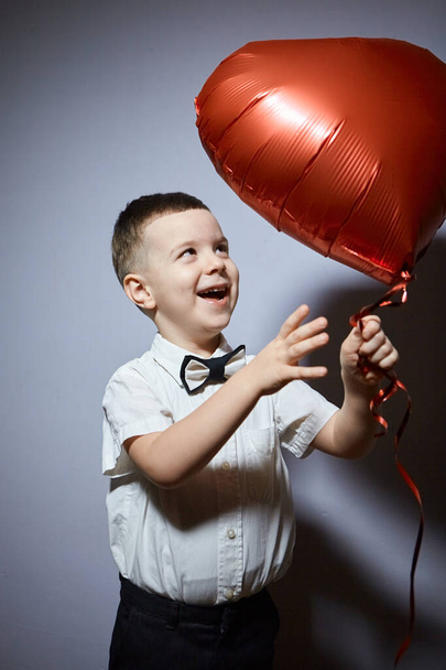 Valentine's day. Happy boy stands and holds red ball hearts on a white background.  - Фото, зображення