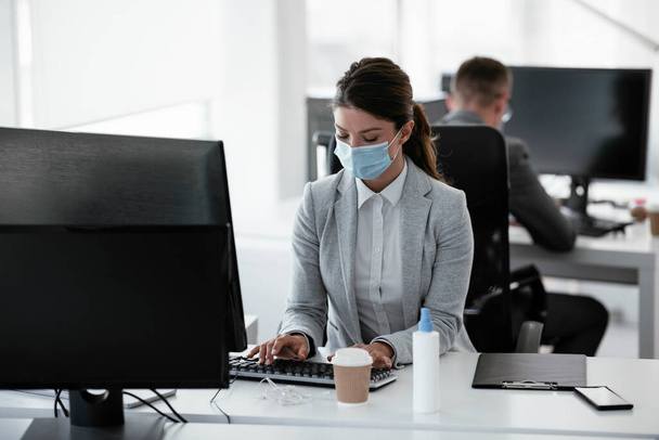 Piękna bizneswoman z maską medyczną pracująca w biurze. Koncepcja Covid-19. - Zdjęcie, obraz
