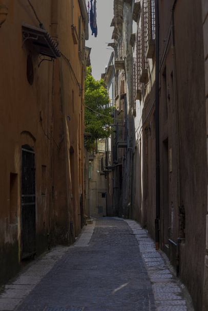 Narrow alley of Sant'Agata dei Goti at sunset with a beam of light in the center and shadows on the houses of the narrow street. - Photo, Image