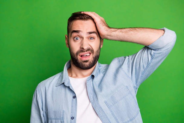 Portrait of upset guy hand head wear blue shirt isolated on vibrant green color background - Фото, зображення