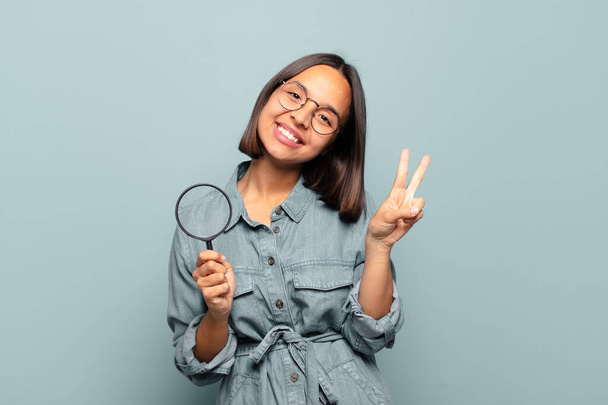 young hispanic woman smiling and looking happy, carefree and positive, gesturing victory or peace with one hand - Фото, изображение