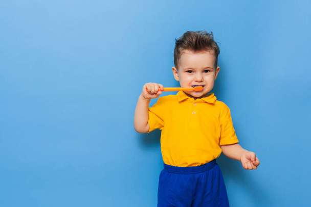Happy child kid boy brushing teeth with toothbrush on blue background. Health care, dental hygiene. Mockup, copy space - Фото, изображение