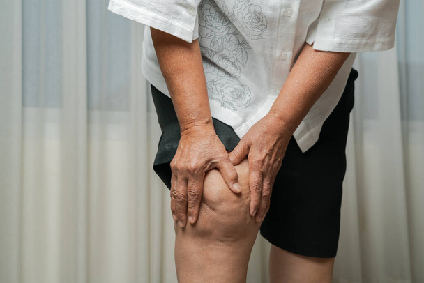 starsza kobieta cierpiąca na ból kolana w domu, koncepcja problemu zdrowotnego - Zdjęcie, obraz