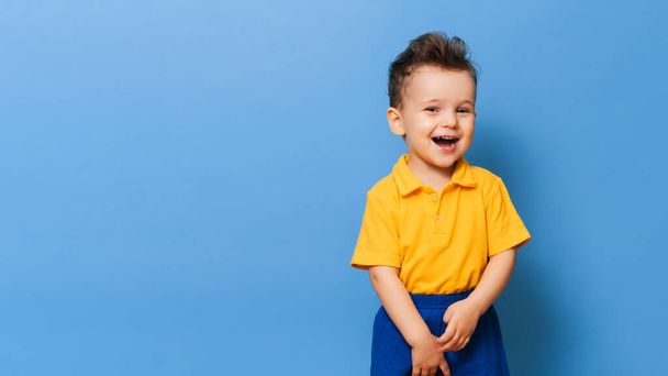 Portret słodkiego, śmiejącego się chłopca na niebieskim tle. Przestrzeń kopiowania. - Zdjęcie, obraz