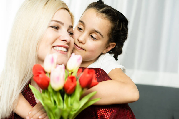 Szczęśliwego Dnia Matki. Dziecko córka gratuluje mamom i daje jej pocztówkę i kwiaty tulipany - Zdjęcie, obraz